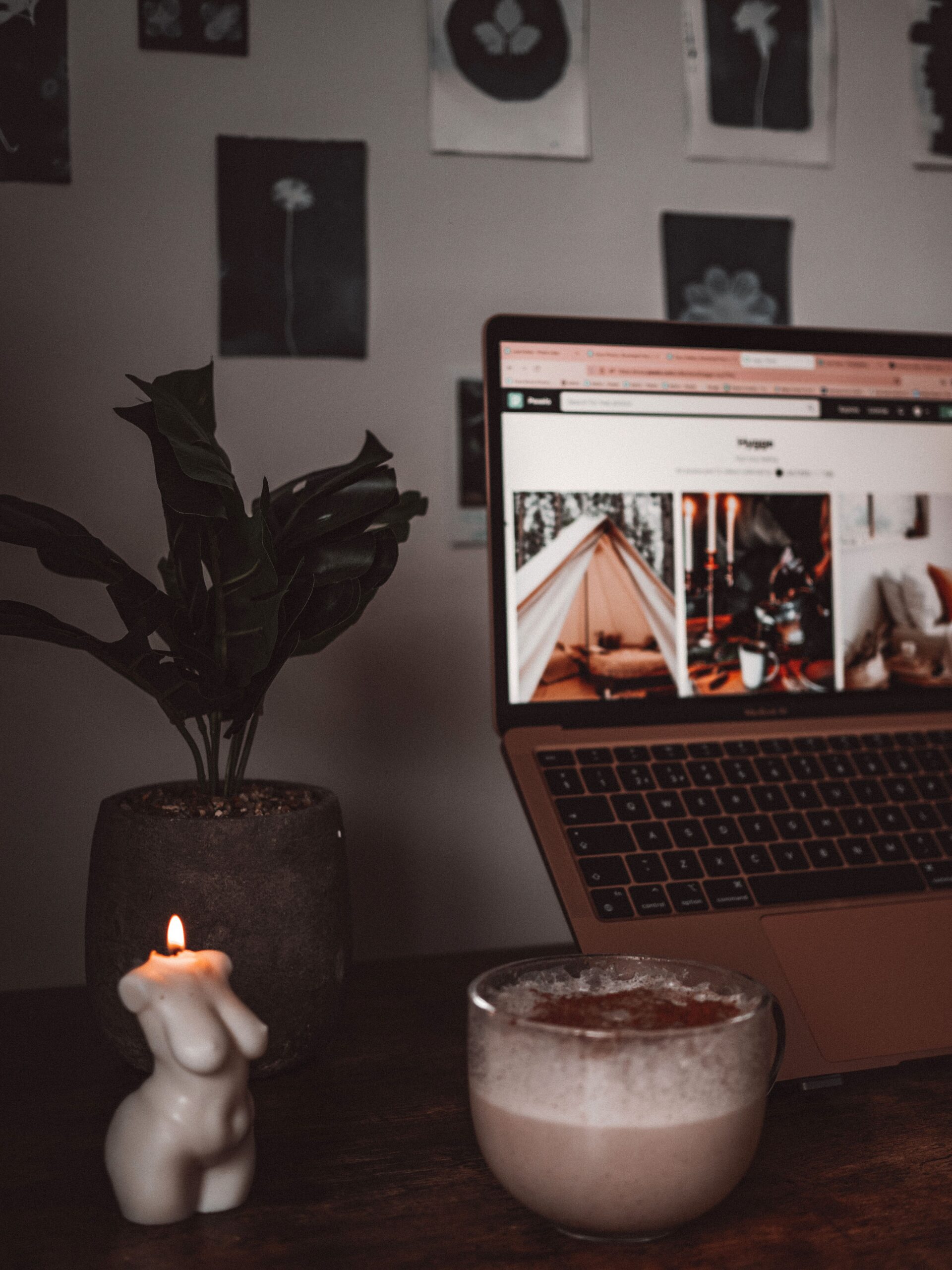 A desk with a laptop next to a cup of coffee and a lit candle.